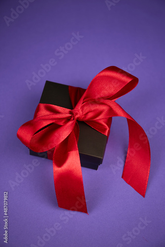 black gift with red ribbon on purple background. Valentine's day. Birthday or Holidays concept. Copy space