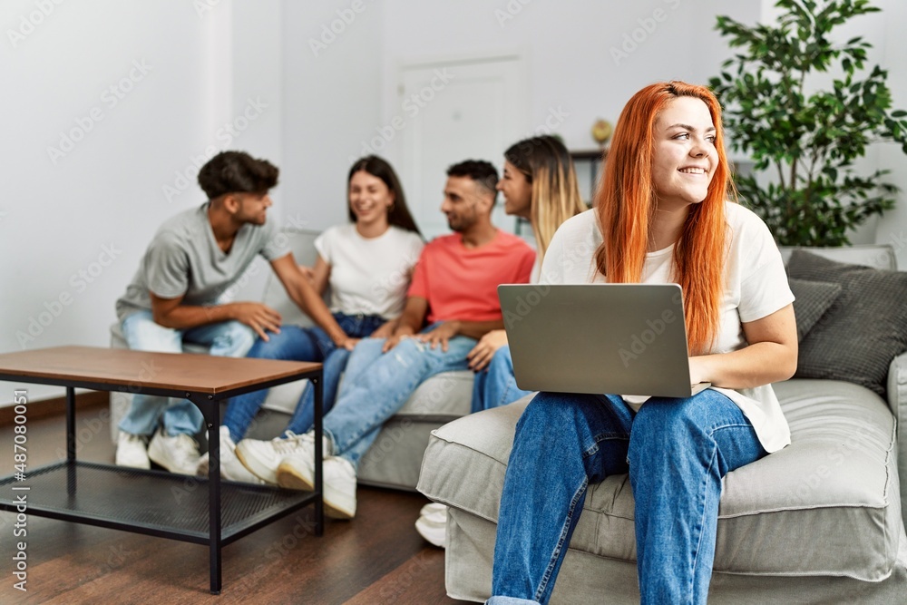 Group of young friends speaking sitting on the sofa. Woman smilimg happy and using laptop at home. Group of young friends speaking sitting on the sofa. Woman smilimg happy and using laptop at home.