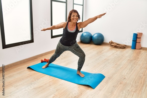 Middle age hispanic sporty woman smiling happy training yoga at sport center.