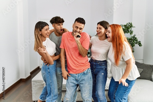 Group of young friends having party singing song using microphone at home.