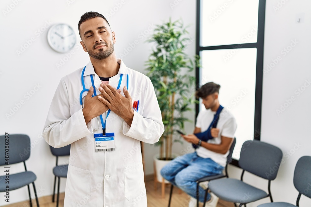 Hispanic doctor man at waiting room with pacient with arm injury smiling with hands on chest with closed eyes and grateful gesture on face. health concept. Hispanic doctor man at waiting room with pacient with arm injury smiling with hands on chest with closed eyes and grateful gesture on face. health concept.