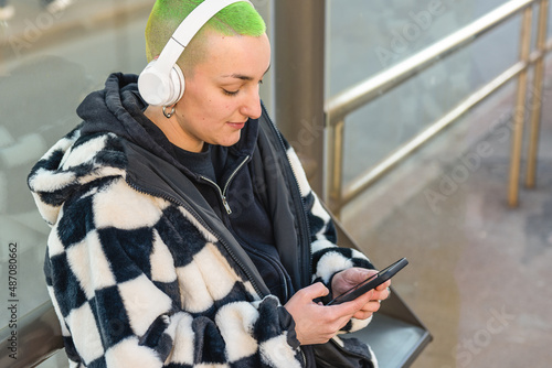 young lesbian woman waiting at the bus stop, choosing and listening music with modern devices, diversity concept of style and gender photo