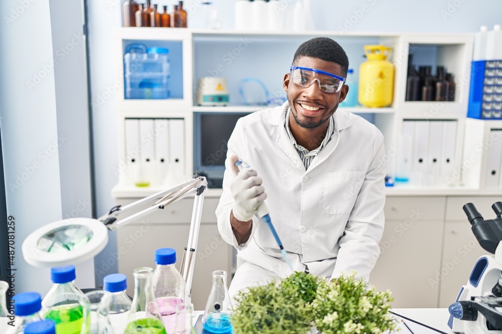 Young african american man wearing scientist uniform using pipette on plant at laboratory Young african american man wearing scientist uniform using pipette on plant at laboratory