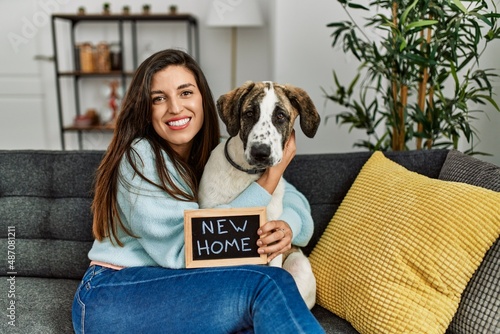 Young woman holding new home blackboard hugging dog sitting on sofa at home