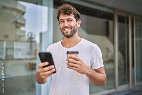 Young hispanic man using smartphone drinking coffee at street