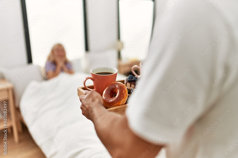 Man surprising his girlfriend with breakfast on the bed at home.