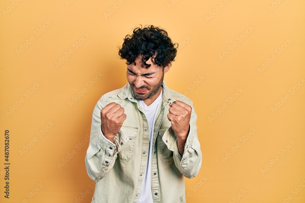 Young hispanic man wearing casual clothes very happy and excited doing winner gesture with arms raised, smiling and screaming for success. celebration concept. Young hispanic man wearing casual clothes very happy and excited doing winner gesture with arms raised, smiling and screaming for success. celebration concept.