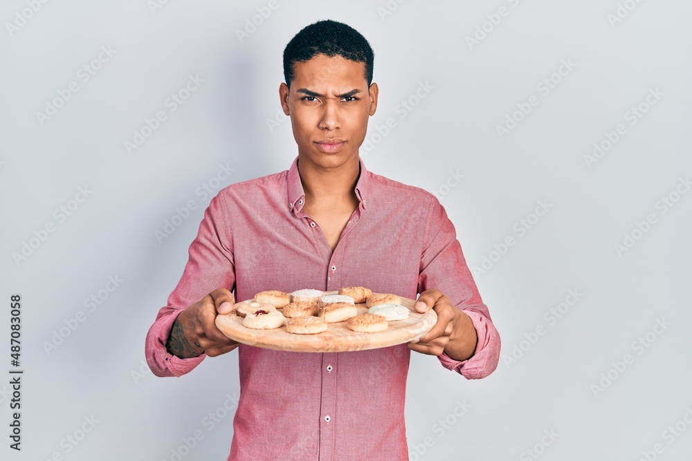 Young african american guy holding tray with cake sweets skeptic and nervous, frowning upset because of problem. negative person. Young african american guy holding tray with cake sweets skeptic and nervous, frowning upset because of problem. negative person.