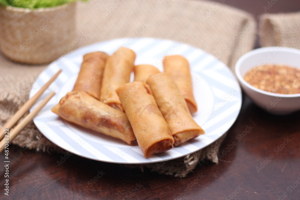 Fried spring rolls with vegetables and tomatoes placed in a black plate on a white wooden table and dipping sauce. Fried spring rolls with vegetables and tomatoes placed in a black plate on a white wooden table and dipping sauce.