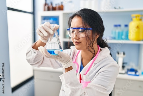 Young chinese woman wearing scientist uniform holding test tube at laboratory