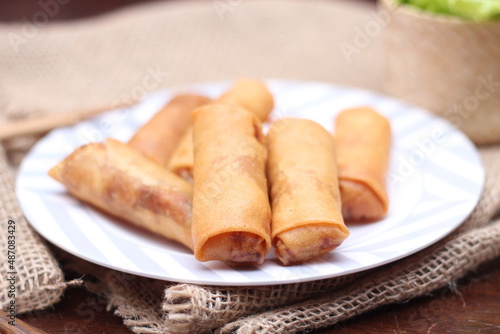 Fried spring rolls with vegetables and tomatoes placed in a black plate on a white wooden table and dipping sauce.