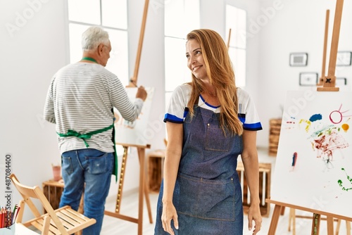 Hispanic woman wearing apron at art studio looking away to side with smile on face, natural expression. laughing confident.