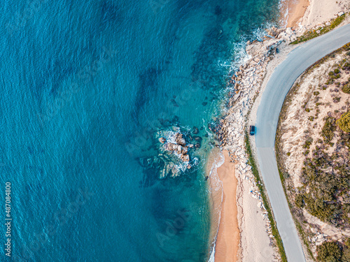 Aerial view of an idyllic sea sandy beach with asphalt winding road and small car driving on. Background for travel and vacation