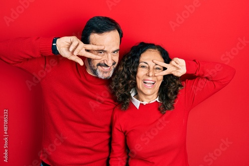 Middle age couple of hispanic woman and man hugging and standing together doing peace symbol with fingers over face, smiling cheerful showing victory © Krakenimages.com