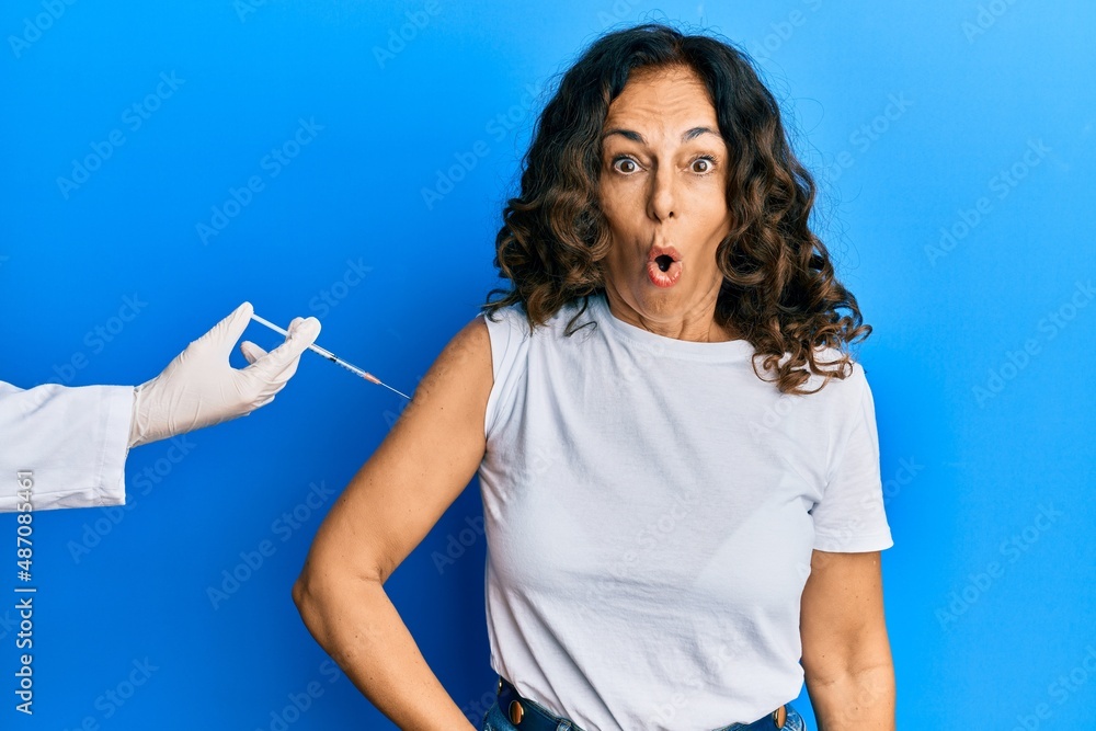 Middle age hispanic woman getting vaccine scared and amazed with open mouth for surprise, disbelief face Middle age hispanic woman getting vaccine scared and amazed with open mouth for surprise, disbelief face