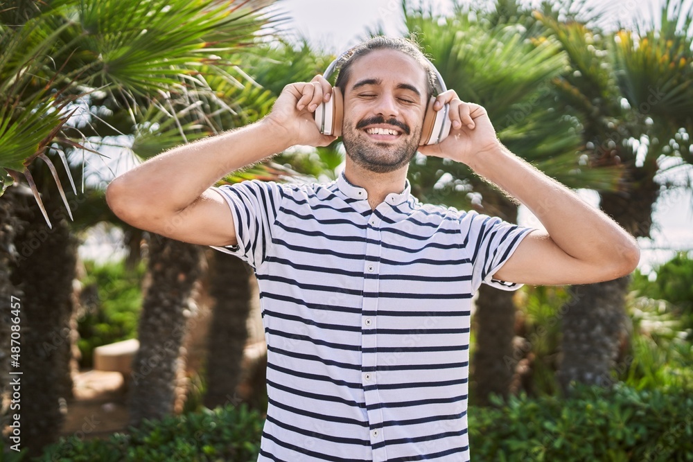 Young hispanic man smiling confident listening to music at park