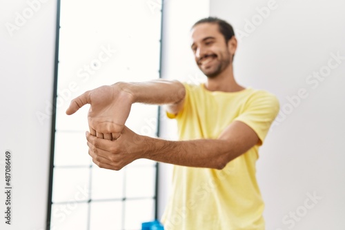 Handsome hispanic man stretching arms at the gym