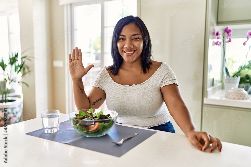 Young hispanic woman eating healthy salad at home showing and pointing up with fingers number five while smiling confident and happy. Young hispanic woman eating healthy salad at home showing and pointing up with fingers number five while smiling confident and happy.