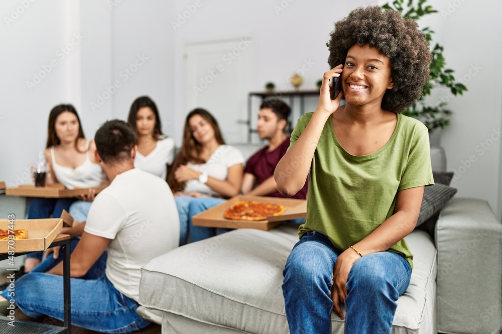 Group of young friends eating italian sitting on the sofa. Woman smiling and talking on the smartphone at home.