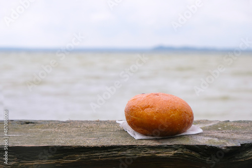 Traditional donut or ponchik on a wooden bench on a lake background. Lake Svityaz, Volyn region, Ukraine. Takeaway food. Copy space.  photo