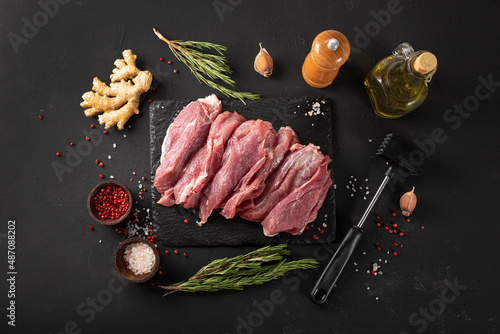 Pieces of fresh pork meat on a black background, raw meat with seasoning for cooking on a black board top view