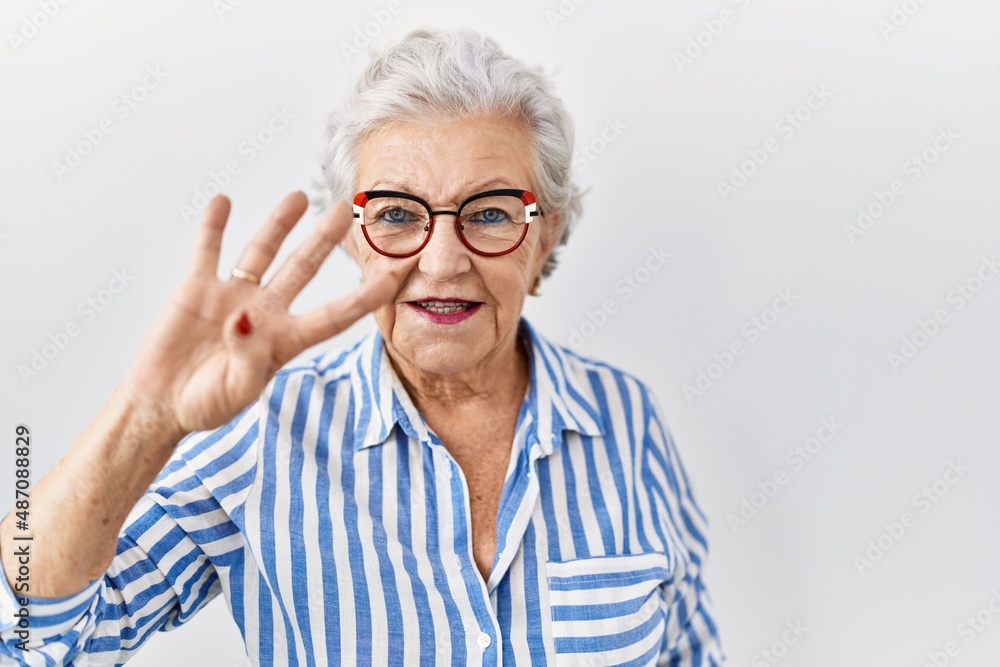 Senior woman with grey hair standing over white background showing and pointing up with fingers number four while smiling confident and happy. Senior woman with grey hair standing over white background showing and pointing up with fingers number four while smiling confident and happy.