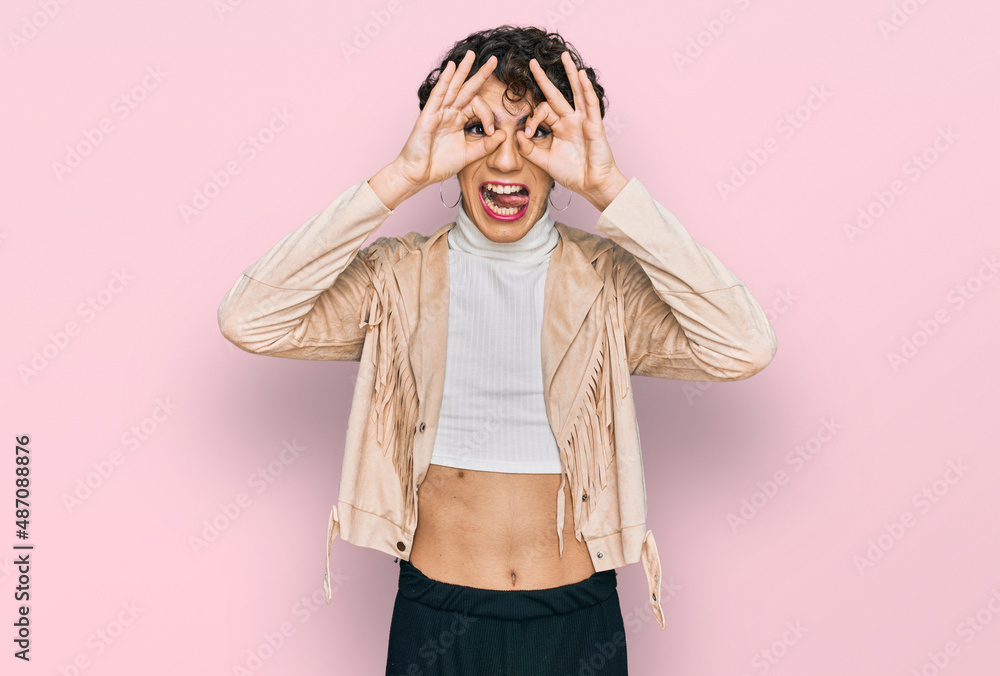 Handsome man wearing make up and woman clothes doing ok gesture like binoculars sticking tongue out, eyes looking through fingers. crazy expression. Handsome man wearing make up and woman clothes doing ok gesture like binoculars sticking tongue out, eyes looking through fingers. crazy expression.