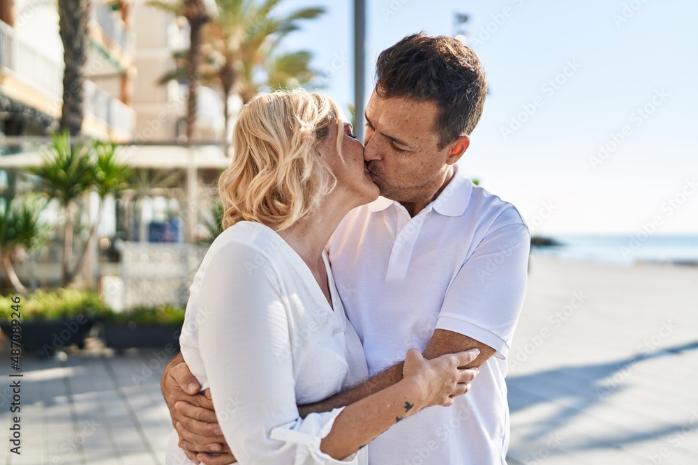 Middle age man and woman couple hugging each other and kissing standing at street Middle age man and woman couple hugging each other and kissing standing at street