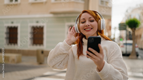 Young redhead woman smiling confident listening to music using smartphone at street