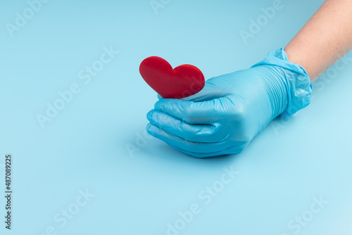 Red heart in hands in blue medical gloves on blue background. Background for the day of the medic. World Heart Day. Heart diseases.