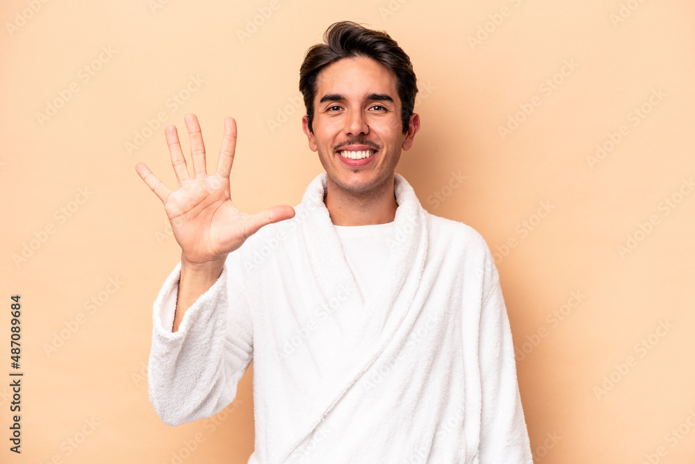 Young caucasian man wearing a bathrobe isolated on beige background smiling cheerful showing number five with fingers. Young caucasian man wearing a bathrobe isolated on beige background smiling cheerful showing number five with fingers.