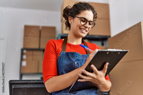 Young latin woman ecommerce business worker writing on clipboard at office photo