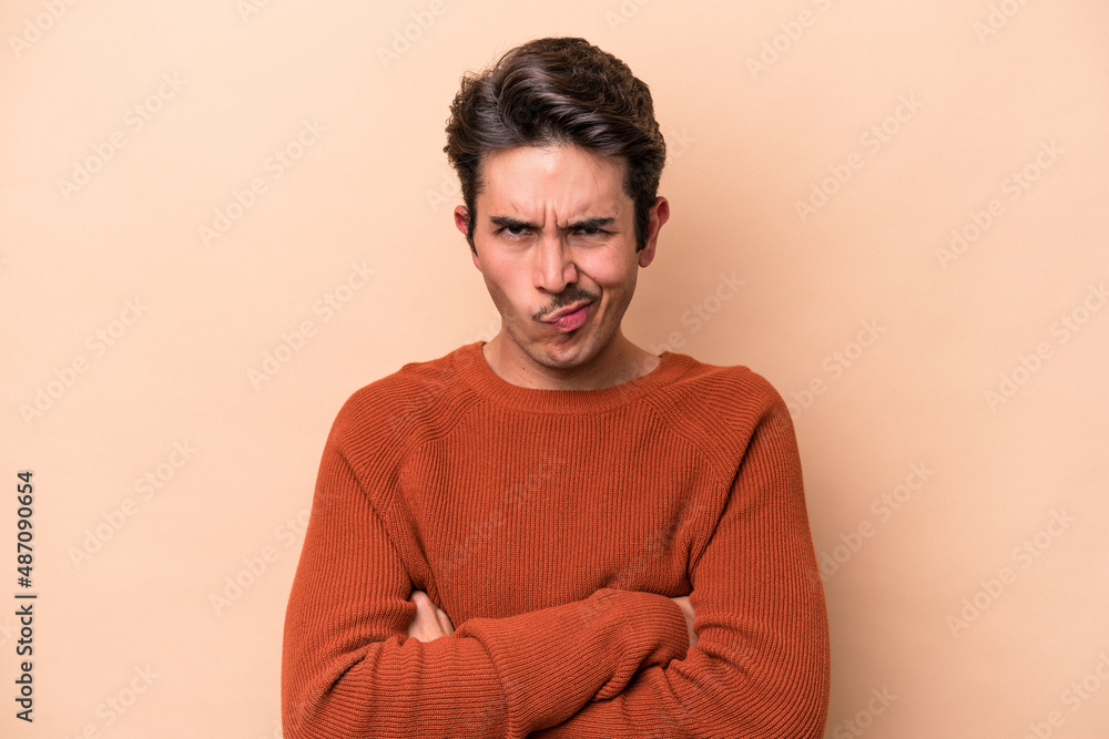 Young caucasian man isolated on beige background frowning face in displeasure, keeps arms folded. Young caucasian man isolated on beige background frowning face in displeasure, keeps arms folded.