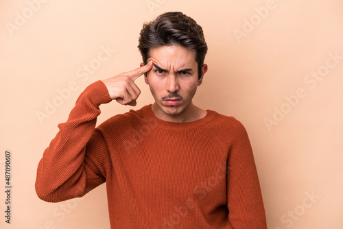 Young caucasian man isolated on beige background pointing temple with finger, thinking, focused on a task. © Asier