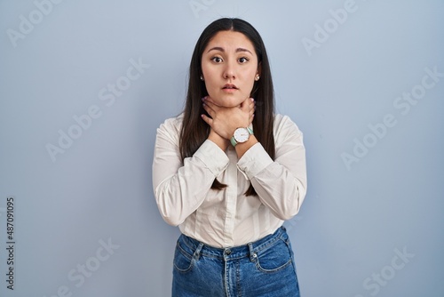 Young latin woman standing over blue background shouting suffocate because painful strangle. health problem. asphyxiate and suicide concept.