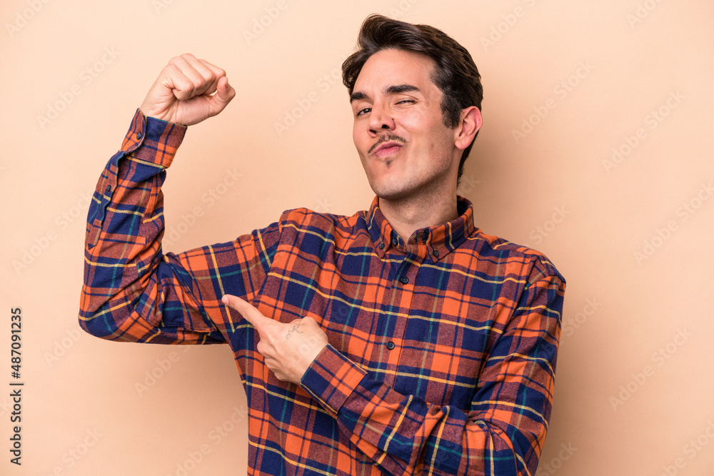Young caucasian man isolated on beige background showing strength gesture with arms, symbol of feminine power Young caucasian man isolated on beige background showing strength gesture with arms, symbol of feminine power