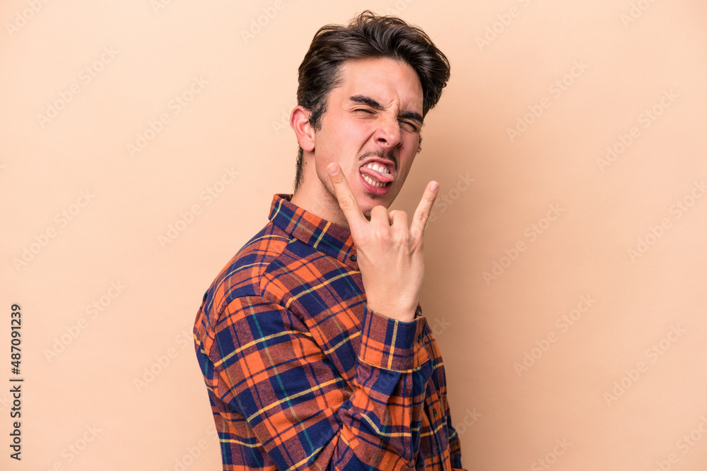 Young caucasian man isolated on beige background showing rock gesture with fingers Young caucasian man isolated on beige background showing rock gesture with fingers