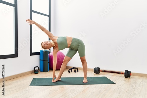 Young blonde girl smiling happy training yoga at sport center.