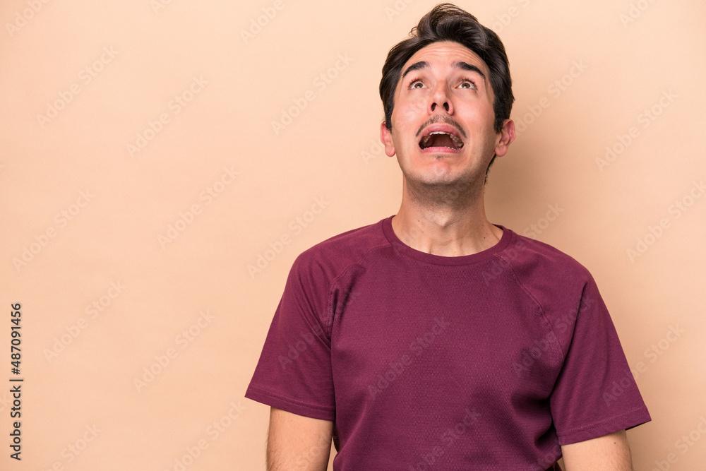 Young caucasian man isolated on beige background shouting very angry, rage concept, frustrated. Young caucasian man isolated on beige background shouting very angry, rage concept, frustrated.