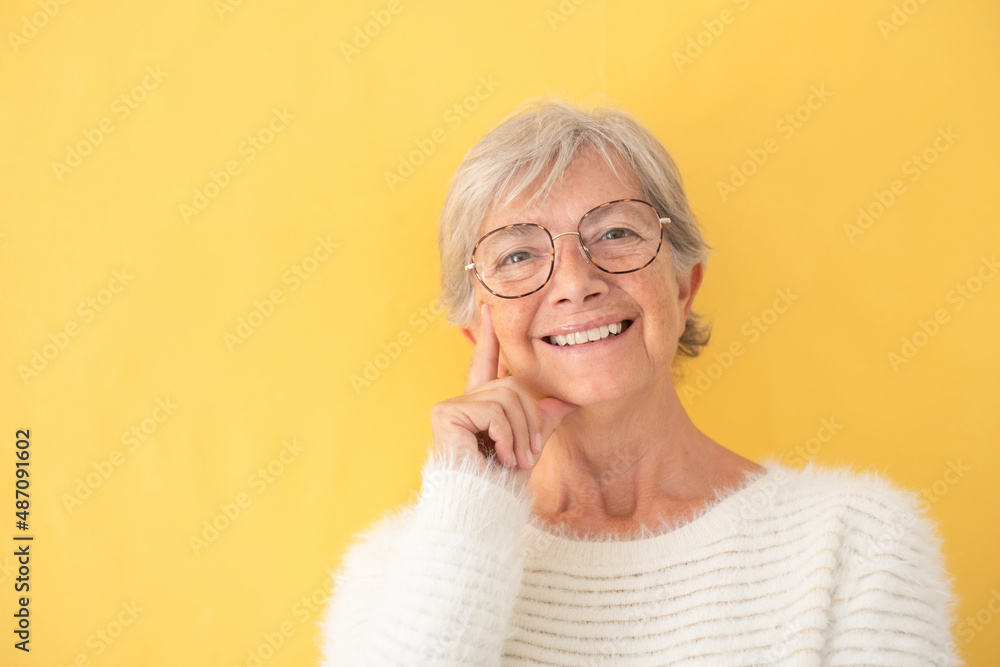 Portrait of beautiful happy mature woman white dressed wearing eyeglasses looking at camera, on yellow background