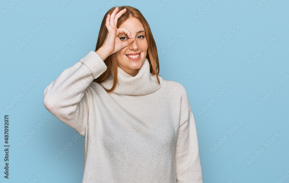 Young irish woman wearing casual winter sweater doing ok gesture with hand smiling, eye looking through fingers with happy face. Young irish woman wearing casual winter sweater doing ok gesture with hand smiling, eye looking through fingers with happy face.