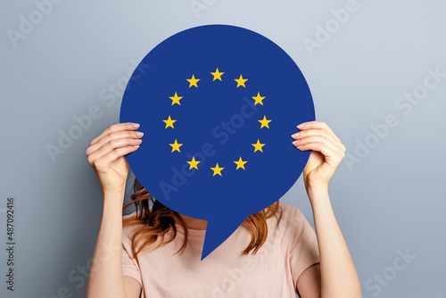 woman holds blank white speech bubble with european union flag isolated over grey studio background. News information channel concept