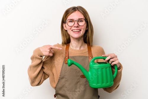 Young gardener woman holding a sprinkler isolated on white background person pointing by hand to a shirt copy space, proud and confident