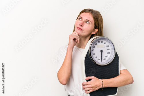 Young English woman holding a scale isolated on white background looking sideways with doubtful and skeptical expression.