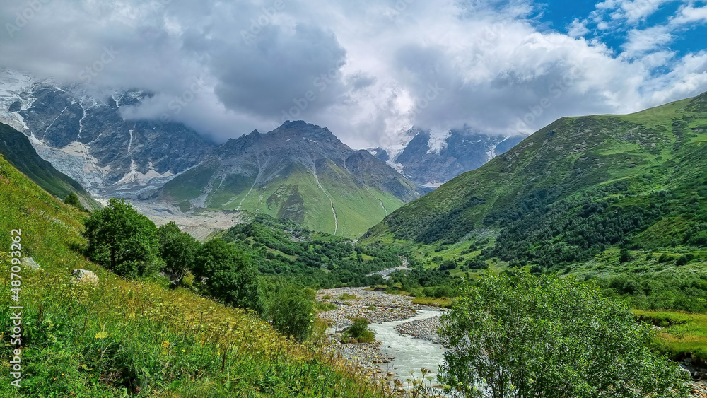 Patara Enguri River flowing down the a valley with view on the Shkhara Glacier in the Greater Caucasus Mountain Range in Georgia, Svaneti Region, Ushguli. Snow-capped mountains in the back. Wilderness