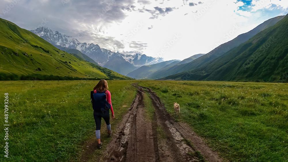A female hiker on a hiking path leading to the Shkhara Glacier in the Greater Caucasus Mountain Range in Georgia, Svaneti Region, Ushguli. Snow-capped mountains in the back. Wanderlust. Wilderness.