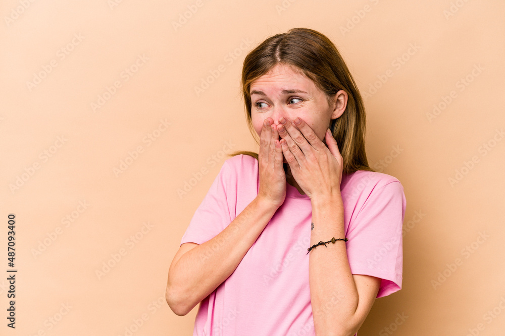 Young English woman isolated on beige background laughing about something, covering mouth with hands. Young English woman isolated on beige background laughing about something, covering mouth with hands.