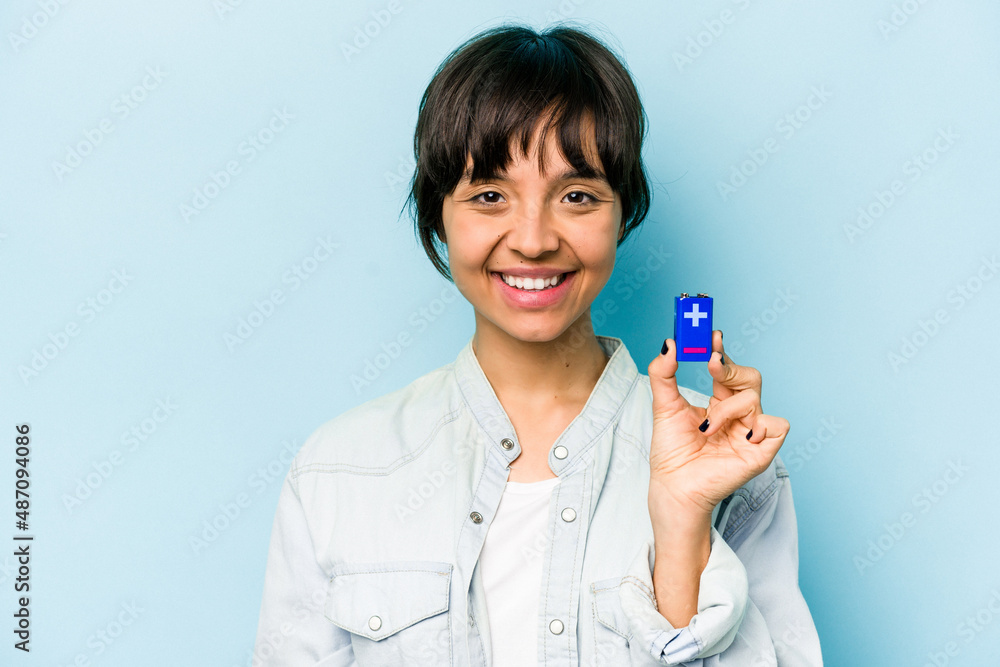 Young hispanic woman holding a batterie isolated on blue background happy, smiling and cheerful. Young hispanic woman holding a batterie isolated on blue background happy, smiling and cheerful.