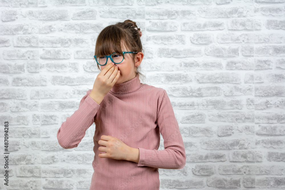 Portrait of frustrated school girl pinching nose with disgust on his face due to bad smell isolated over gray brick wall background. smelling something stinky and disgusting, intolerable smell. Portrait of frustrated school girl pinching nose with disgust on his face due to bad smell isolated over gray brick wall background. smelling something stinky and disgusting, intolerable smell.