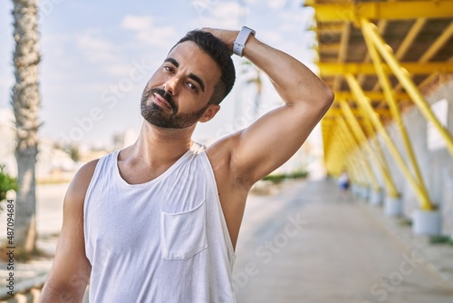Hispanic man stretching neck after working out outdoors on a sunny day